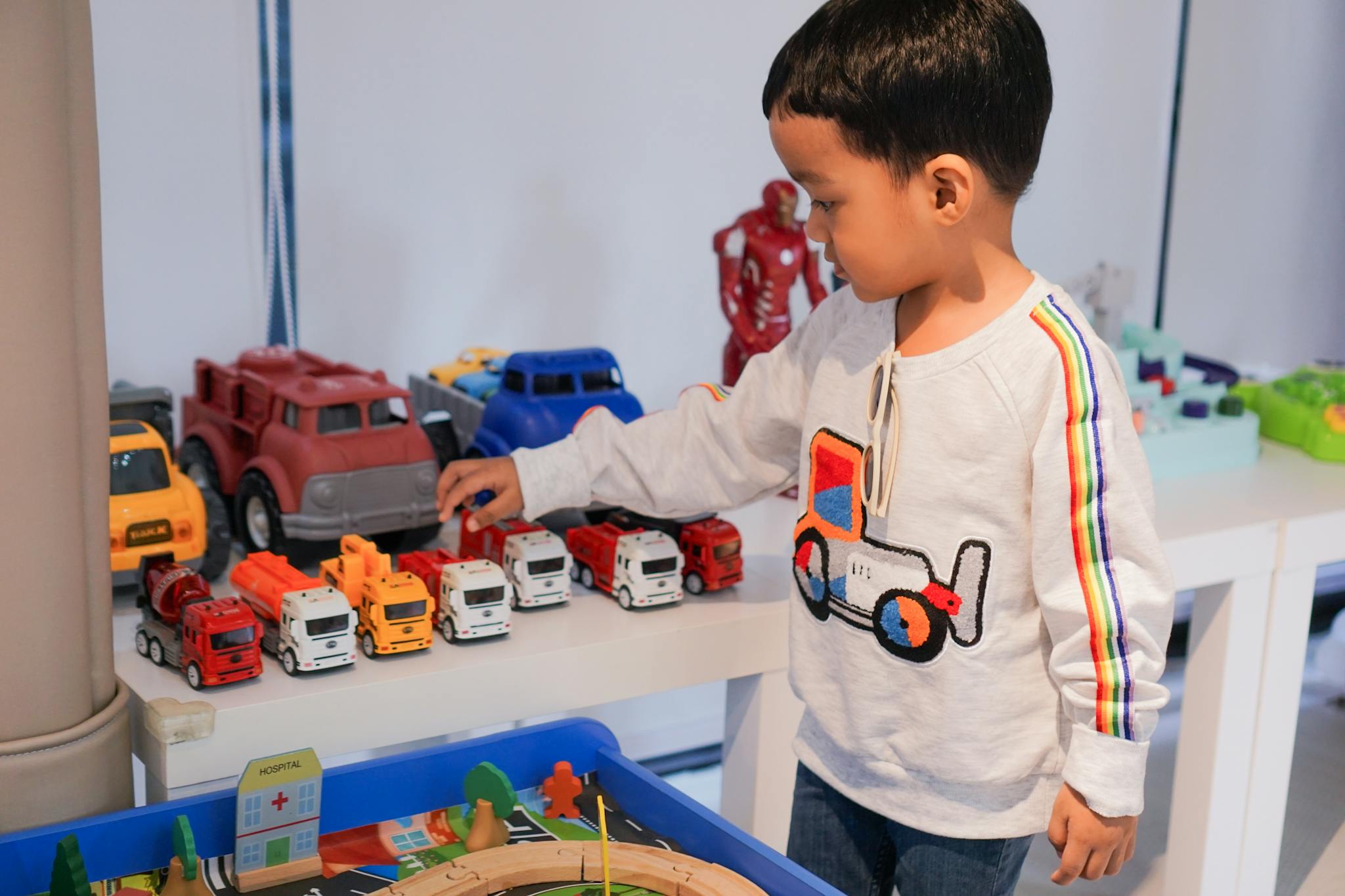 A young boy playing indoors with colorful toy trucks on a table, focused and imaginative.