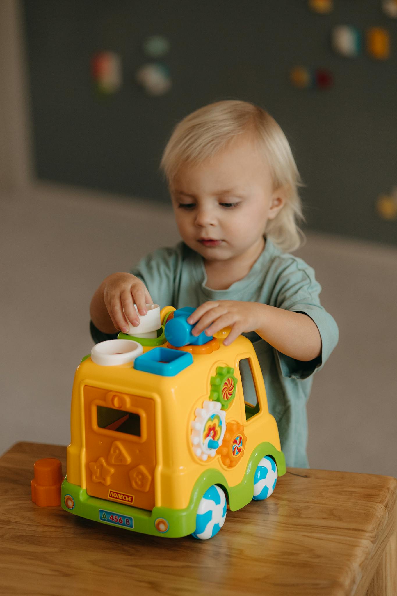Young child engaging with a vibrant toy truck indoors, showcasing curiosity and playfulness.